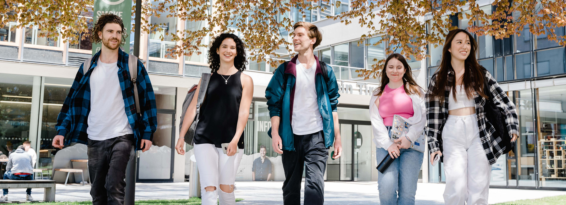 Fünf Studierende gehen gemeinsam über den Campus bei Frühlingswetter