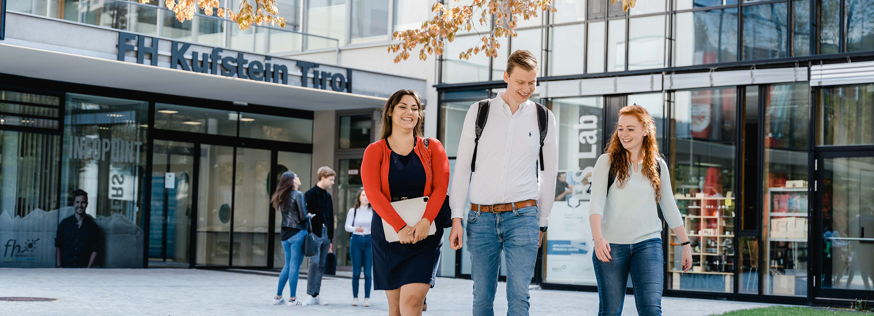All Inclusive Package | © FH Kufstein Tirol Drei Personen gehen vor einem modernen Gebäude mit der Aufschrift FH Kufstein Tirol | © FH Kufstein Tirol